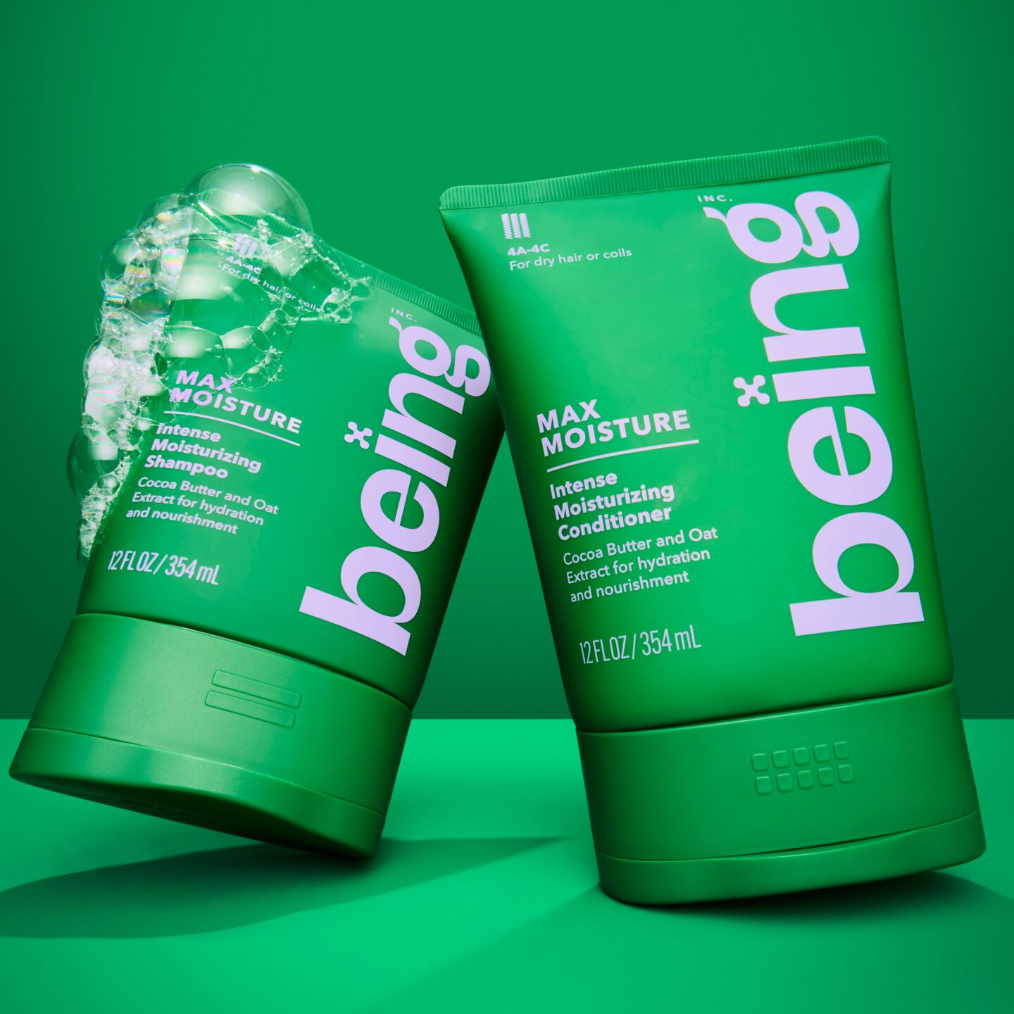 Dos botellas verdes de champú y acondicionador hidratante intenso "being" Max Moisture, con burbujas en la botella de champú, sobre un fondo verde.